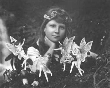 The 1917 Cottingley Fairies photograph: a young girl resting her chin on her hand, with paper cut-out fairies dancing in front of her.